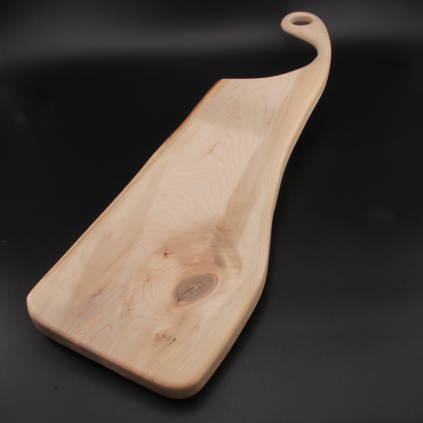 Handcrafted maple charcuterie board with live edge and sweeping handle featuring a hanging loop