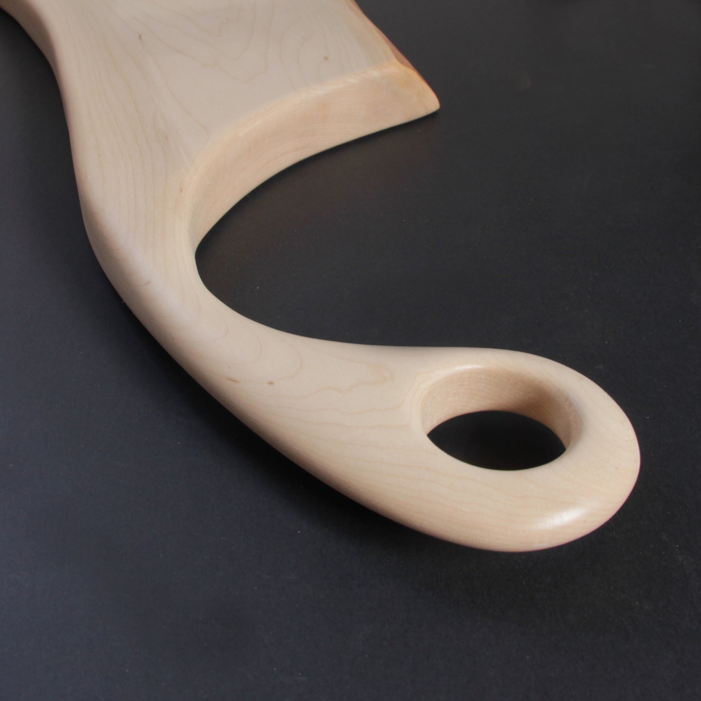 Detail of sweeping maple handle with smooth curve and natural fiber hanging loop