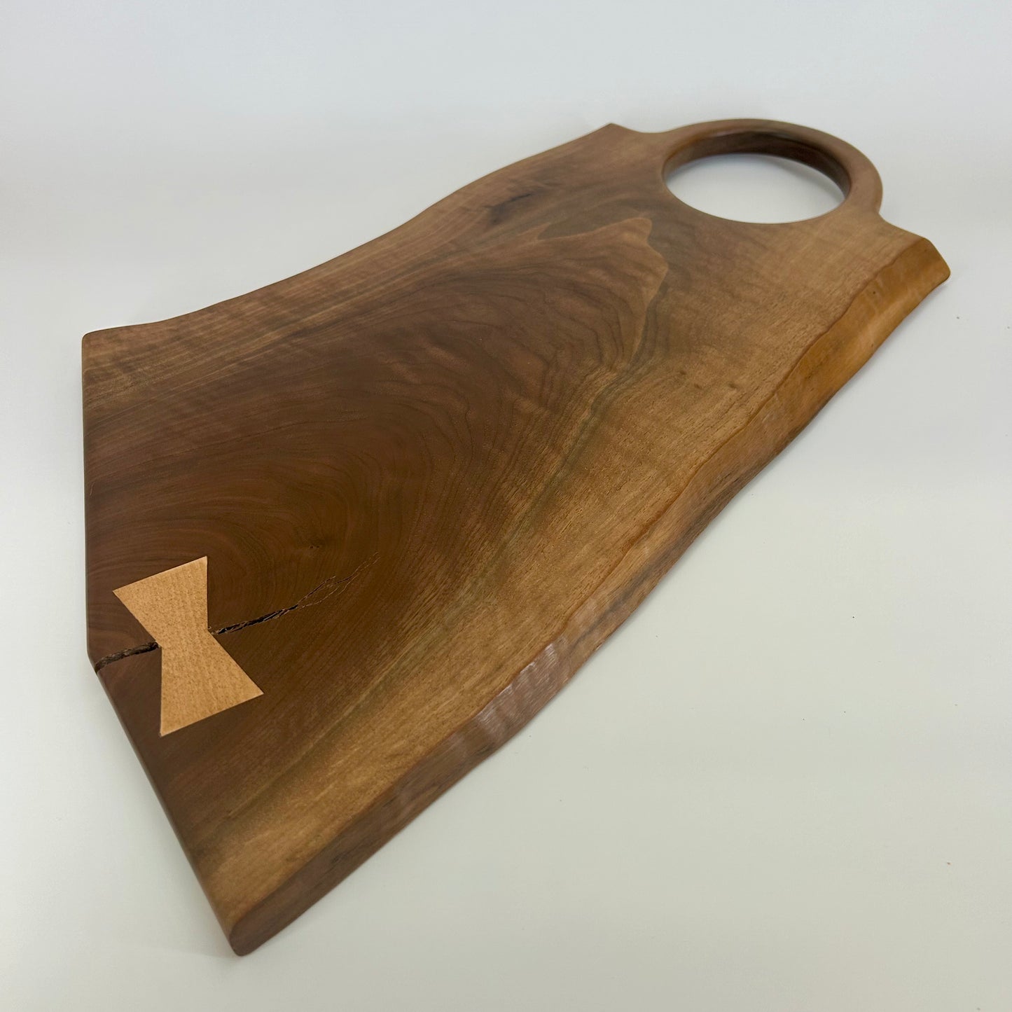Handmade black walnut serving board with natural live edge and round cutout handle